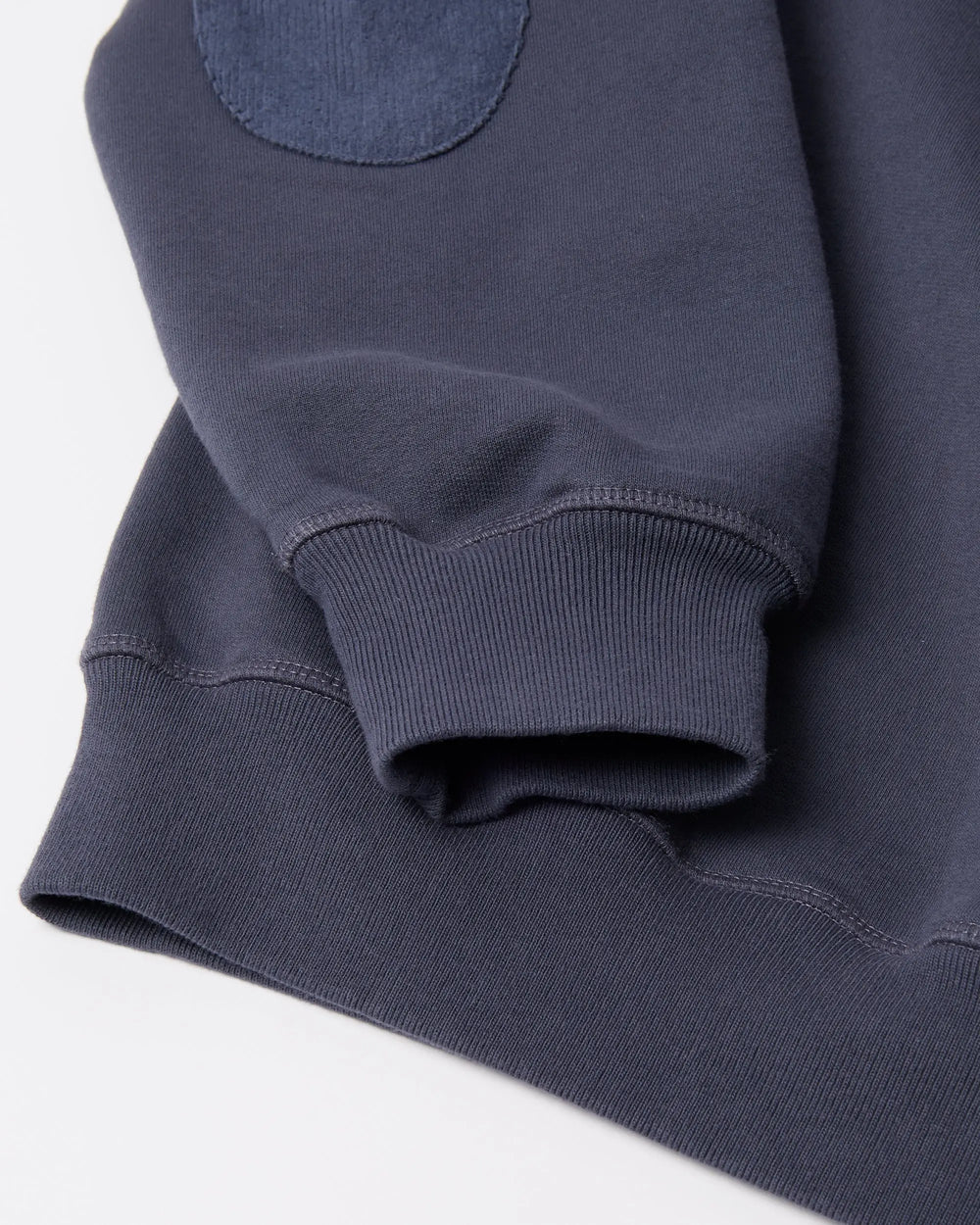 Detail of the ribbed cuff and elbow patch on a navy blue byParra Tired Champione crew neck sweatshirt.